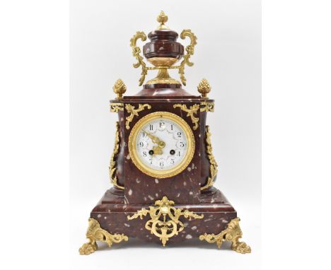 A late 19th century French red marble mantle clock, the case having gilt metal mounts with urn shaped top flanked by the bask