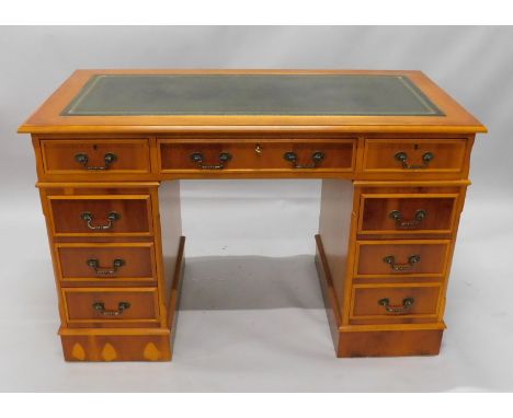 A yew veneered pedestal desk, the rectangular top with a green leather insert, above an arrangement of nine drawers, on a pli