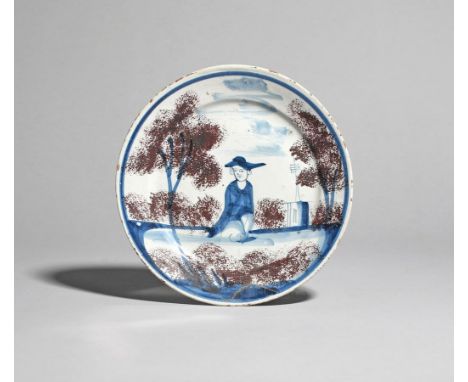 A delftware plate  c.1730, probably Bristol, painted in blue with a central seated figure wearing a large hat, before a build