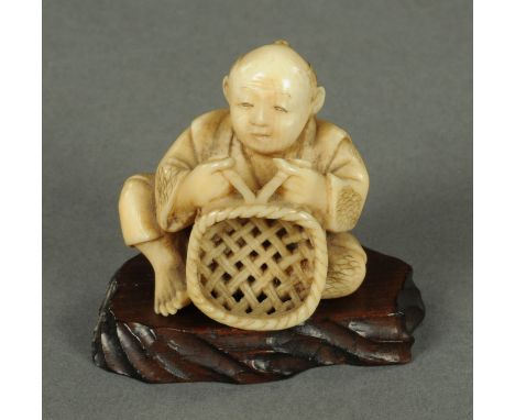 A Japanese ivory Netsuke, of a basket weaver, Meiji period, modelled seated, putting the final weaves to a shallow basket, si