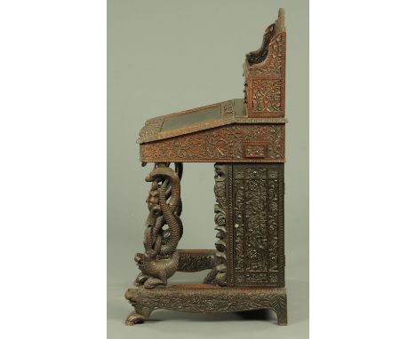 An Anglo-Indian carved hardwood Davenport desk, the superstructure carved with a battle scene and the slope front with mythic