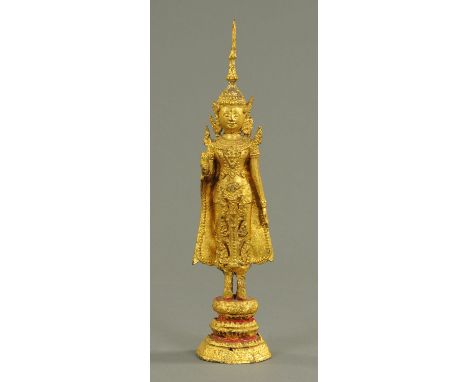 A Thai gilt metal figure standing Buddha, 20th century, in Abhaya Mudra, standing on a raised gilded and red enamel lotus tie