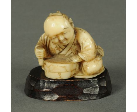 A Japanese carved ivory Netsuke, Meiji period, carved as a seated figure, smoothing a grindstone, with wood stand. Netsuke 2.