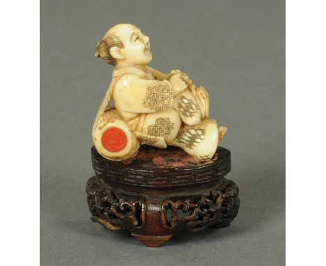 A humorous Japanese ivory Netsuke, Meiji period, a man bending over to tie his sandals, a drum tied onto his back, the red la