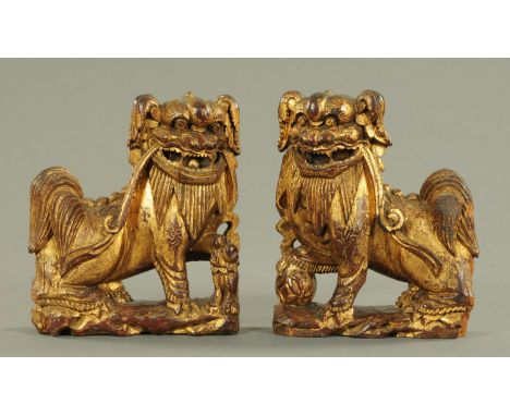 A pair of carved gilded wood Dogs of Fo, 19th century, each with a ribbon in its mouth resting on its haunches, one with its 
