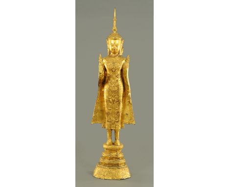 A Thai gilt metal standing Buddha, 20th century, standing in Abhaya Mudra, standing on a flowering lotus upon three stepped t