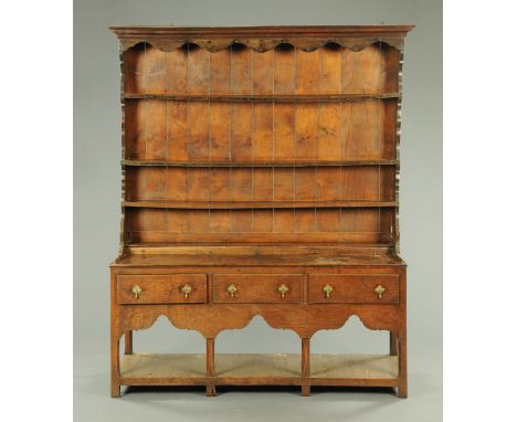 An 18th century oak dresser, with moulded cornice above a series of open shelves, the base fitted with three drawers with sha