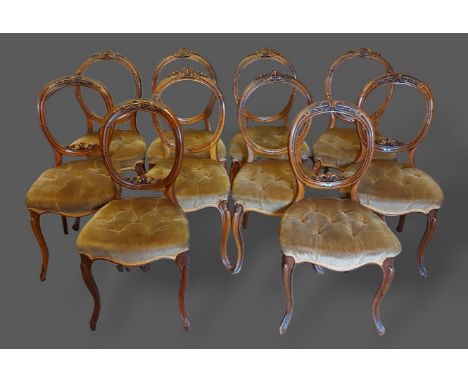 A set of six Victorian walnut balloon back dining chairs, each with a carved back above a button upholstered seat and raised 