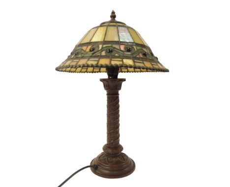 A Tiffany style table lamp, the leaded glass shade of tapering form, with a cast metal base decorated with leaves, on a stepp