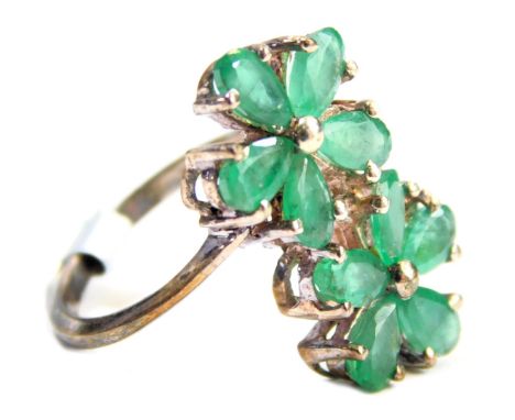 A Coloured Rocks dress ring, formed as two five point floral clusters, each set with emeralds, on white metal stamped 925, ri