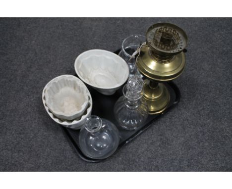 A tray of glass decanters, three vintage jelly moulds, brass oil lamp