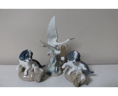 A pair of Nao figures of playful puppies and a Nao figure of a pair of storks in flight. 