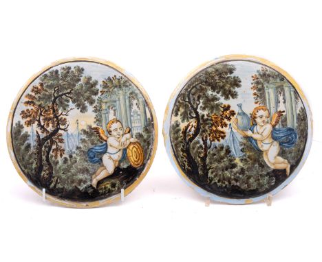 A pair of Castelli maiolica roundels, mid 18th century painted with cupid in a classical landscape with ruins and river beyon
