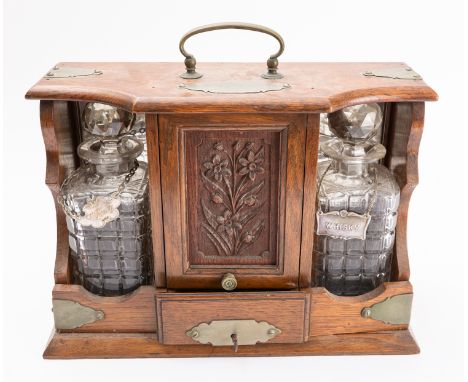 An oak and metal mounted tantalus, late 19th /early 20th century; the shaped top with carrying handle; the front with an uphi