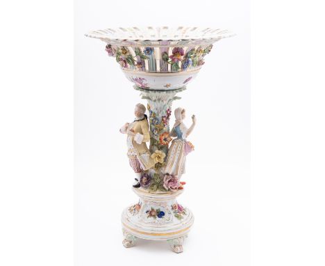 A Carl Thieme porcelain figural comport, modelled with a dandy and companion flanking a flower encrusted trunk supporting a p