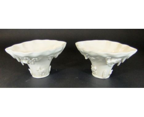 A pair of Chinese blanc-de-chine libation cups in the form of a rhinoceros horn and relief decorated with prunus blossom, dra