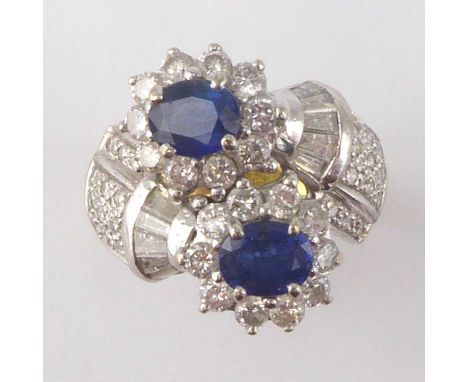 A vintage Art Deco style sapphire and diamond cross-over ring, with two claw set oval sapphires in a border of small claw set