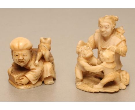 TWO JAPANESE IVORY NETSUKE, one carved as a Samurai holding a palmette fan in his right hand, adjudicating two small wrestlin