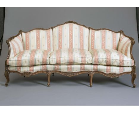 A LOUIS XVI STYLE WALNUT FRAMED SOFA of serpentine outline carved with flowers and scroll work and upholstered in a pale gree