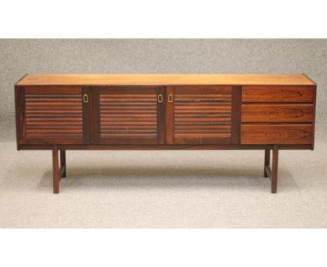 A SCANDINAVIAN ROSEWOOD SIDEBOARD, 1960's, the fascia with three doors with slatted panels and brass drop handles, flanked to