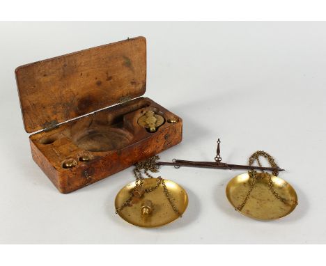A SET OF ANTIQUE BRASS AND IRON WEIGHING SCALES and weights in a dug out wooden box. 8ins long.