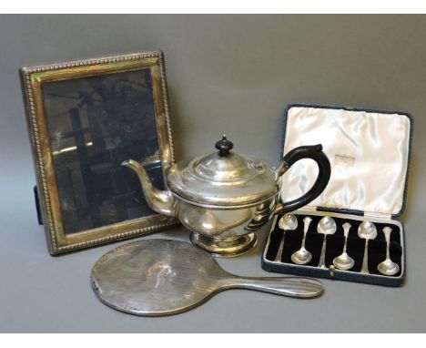 A silver teapot, a hand mirror, an easel back photograph frame, and a cased set of six spoons