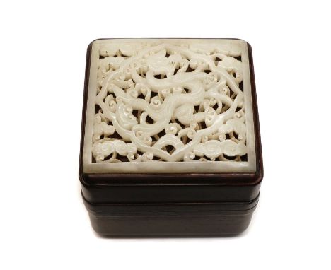 A Chinese jade plaque, pierced and carved with a dragon among clouds, 8cm long, fixed on the cover of a wood box, 8.5cm wide,