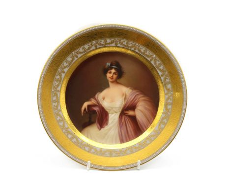 A Vienna porcelain plate, c.1900, decorated with a seated lady in a dress enclosed by a gilt and enamelled border, gilt title
