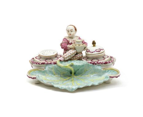A Hochst porcelain inkstand, having central figural support, flanked by inkwell and pot, on a leaf form base, 26cm wide, 14cm