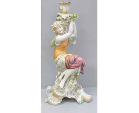 A continental porcelain figural candlestick modelled as a girl seated on a tree stump holding up a bunch of grapes, 25cm 