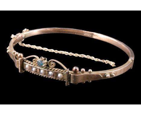 A cased late Victorian sapphire and seed pearl set 9 ct gold bangle, having a sapphire brilliant set between open scrolls abo
