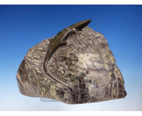 A SERPENTINITE CARVING OF A LIZARD, IT'S BODY POLISHED AGAINST THE ROUGH HEWN ROCK BOULDER, INITIALLED J C.   W 25cms.