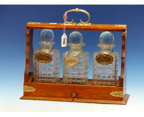 AN OAK THREE BOTTLE TANTALUS, EACH DECANTER WITH ITS LABEL, BRANDY, SHERRY AND SCOTCH.