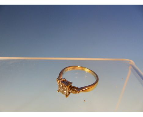 AN 18ct WHITE GOLD DIAMOND RING. THE CENTRAL SETTING FEATURES FOUR PRINCESS CUT DIAMONDS IN A FOUR CLAW SETTING FLANKED BY A 