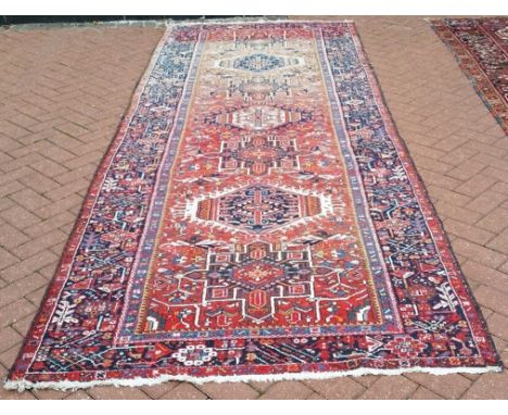 A Persian carpet, with repeating motifs, on a red ground, within a multi border, 378 x 138 cm