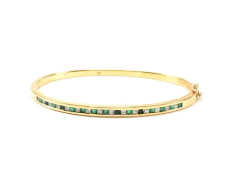 An 18ct gold, emerald and diamond hinged bangle. The bangle having fifteen channel set princess cut diamonds and fifteen chan