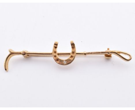 A hallmarked 9ct gold and diamond riding crop and horseshoe brooch pin. The 9ct yellow gold equestrian brooch pin in the form