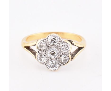 An early 20th-century 18ct gold and diamond cluster ring. The ring set with seven old cut diamonds to bifurcated shoulders an