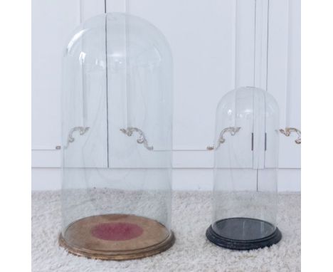 Two large glass domes with wooden circular bases, the largest 73cm high (2)Please note this item is at an offsite location, b
