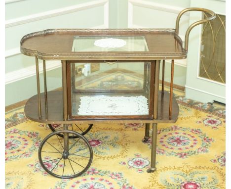 An early 20th century oak drinks trolley, the shaped top with a central moulded glass insert and brass pierced gallery, on wh