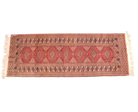 An Afghan style runner, with a design of red lozenges, on a coral ground with one wide and two narrow borders.