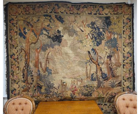 A late 19th / early 20th century French tapestry depicting a woodland scene with trees and flowers with a floral border woven