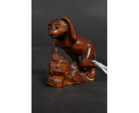 A carved wooden Japanese netsuke in the form of a monkey atop rocks, with inset eyes