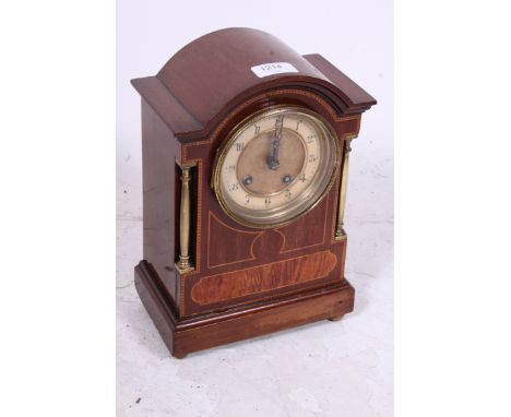 An Edwardian mahogany inlaid and brass bound mantel clock. THe brass movement striking on a chime, with brass columns to side
