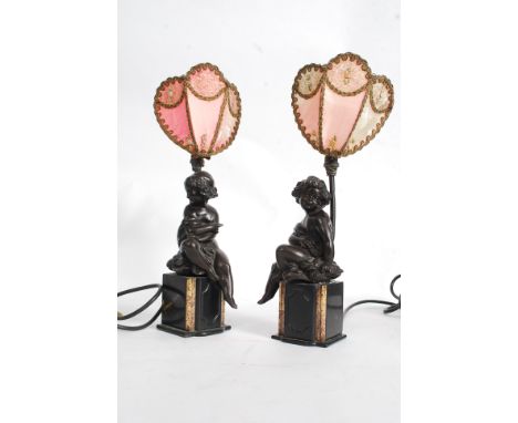 A pair of early 20th century bronze clock garnitures depicting cherubs, being later converted to lamps. Fitted with Art Deco 