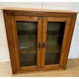 A distressed pine two door glazed cabinet opening to two shelves (H92cm D32cm W90cm)