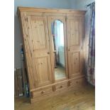 A pine wardrobe comprising of central mirrored door flanked by two panel doors with three drawers