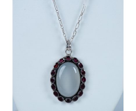 The pendant has a large moonstone in the center surrounded by smaller garnet stones. It measures approximately 2.5"L x 1.25"W