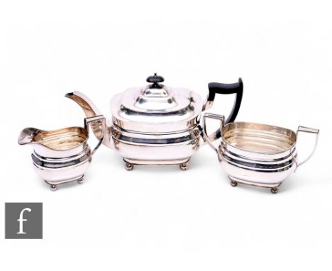 An early 20th Century three-piece boat-shaped silver tea service raised to ball feet, the teapot with ebonised handle and fin