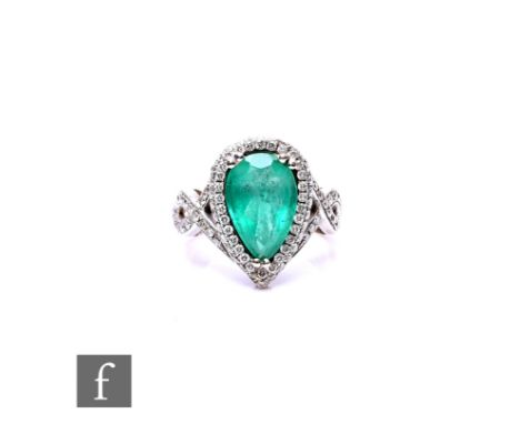 An 18ct white gold emerald and diamond cluster ring, central pear shaped emerald, length 13mm, within a border of diamonds te